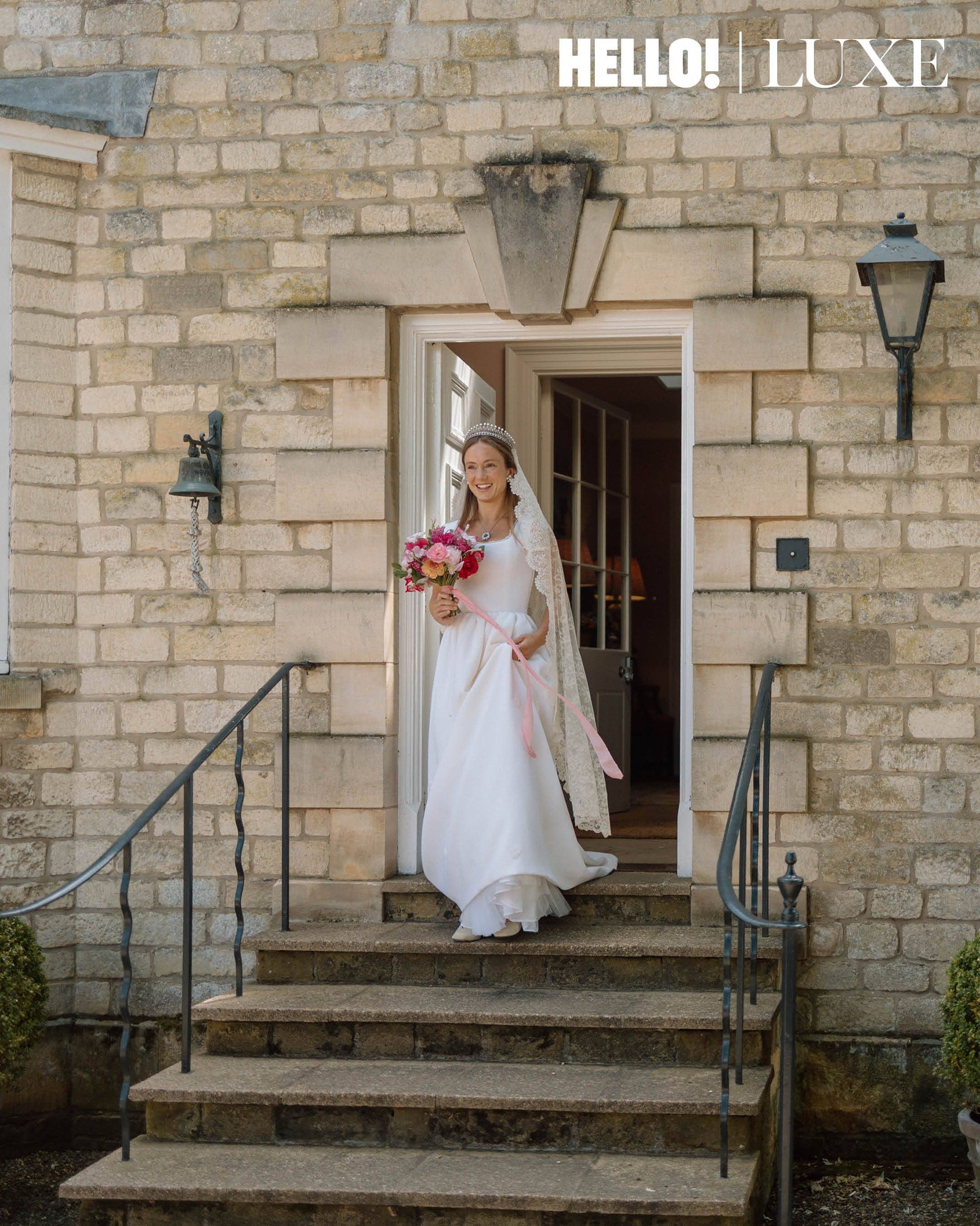 Ready to say "I do": Looking absolutely radiant, the bride beams with joy as she steps out of the doorway of Hovingham Hall, carrying her vibrant summer bouquet and wearing her magnificent antique lace veil