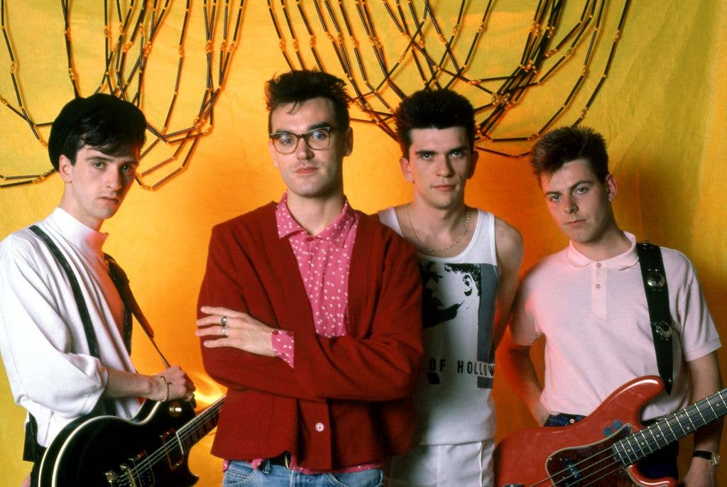 English guitarist Johnny Marr, English singer Morrissey, English drummer Mike Joyce and English bassist Andy Rourke of The Smiths pose for a portrait before their first show in front of a yellow backdrop and selection of cables.