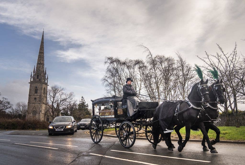 A horse-drawn carriage carrying the coffin of The Vivienne following the funeral of The Vivienne at St Margaret's Church, Bodelwyddan, Denbighshire.