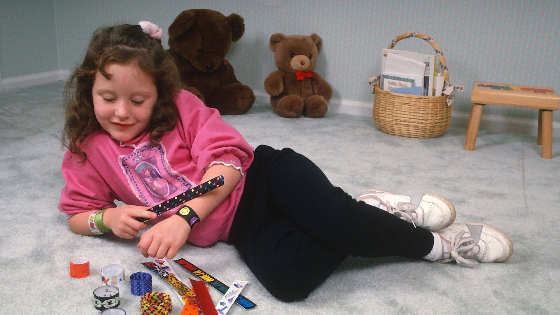 A young girl lying in a bedroom with several slap bracelet toys