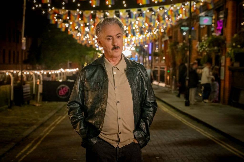 A man stands with hands in pockets in a lit street