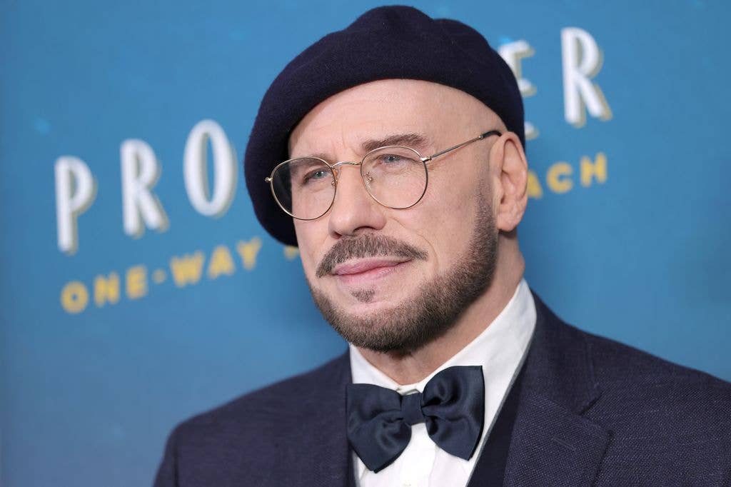 John Travolta in a suit and bowtie with round glasses and a black beret.