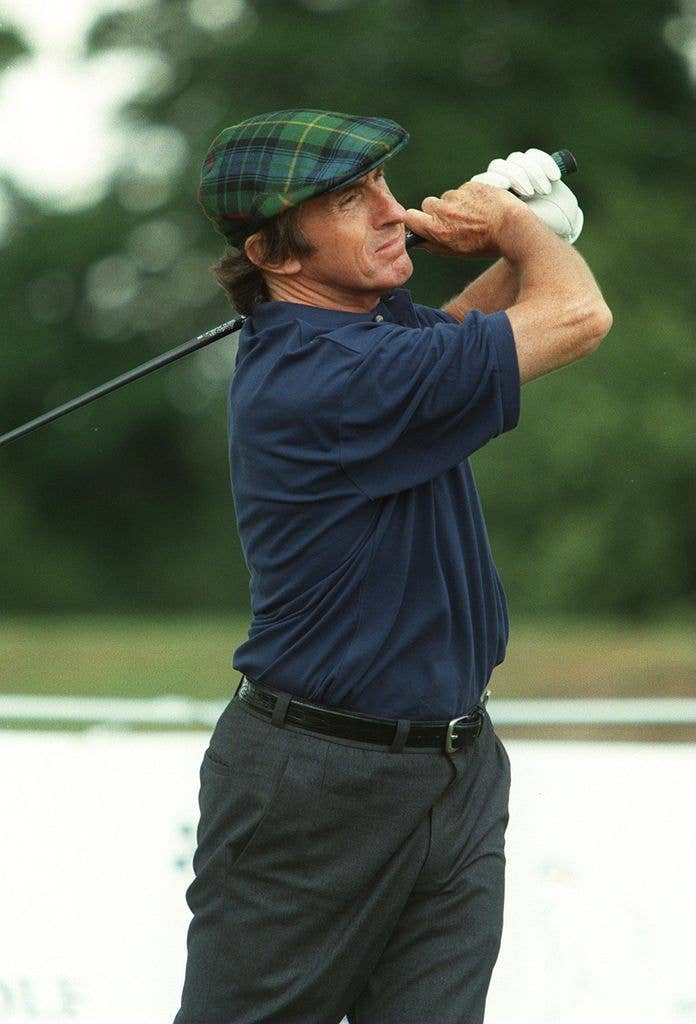 Jackie Stewart holds his golf club over his shoulder and follows the path of his shot.