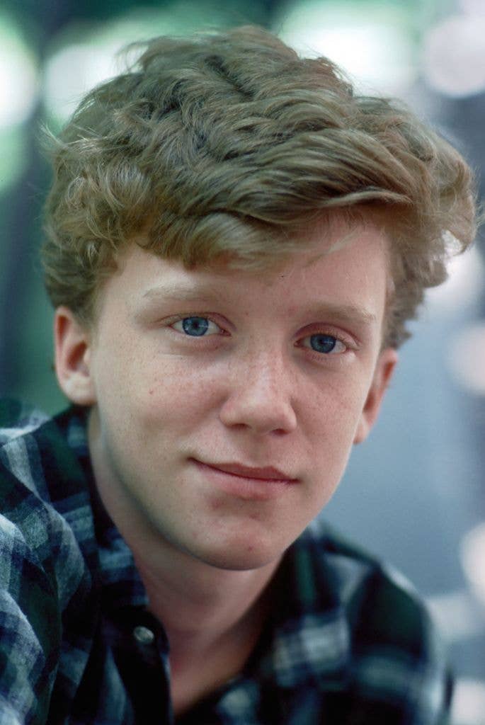 Headshot of Anthony Michael Hall in 1984 wearing a blue check shirt and turning his left shoulder into the camera, looking directly at the lens.