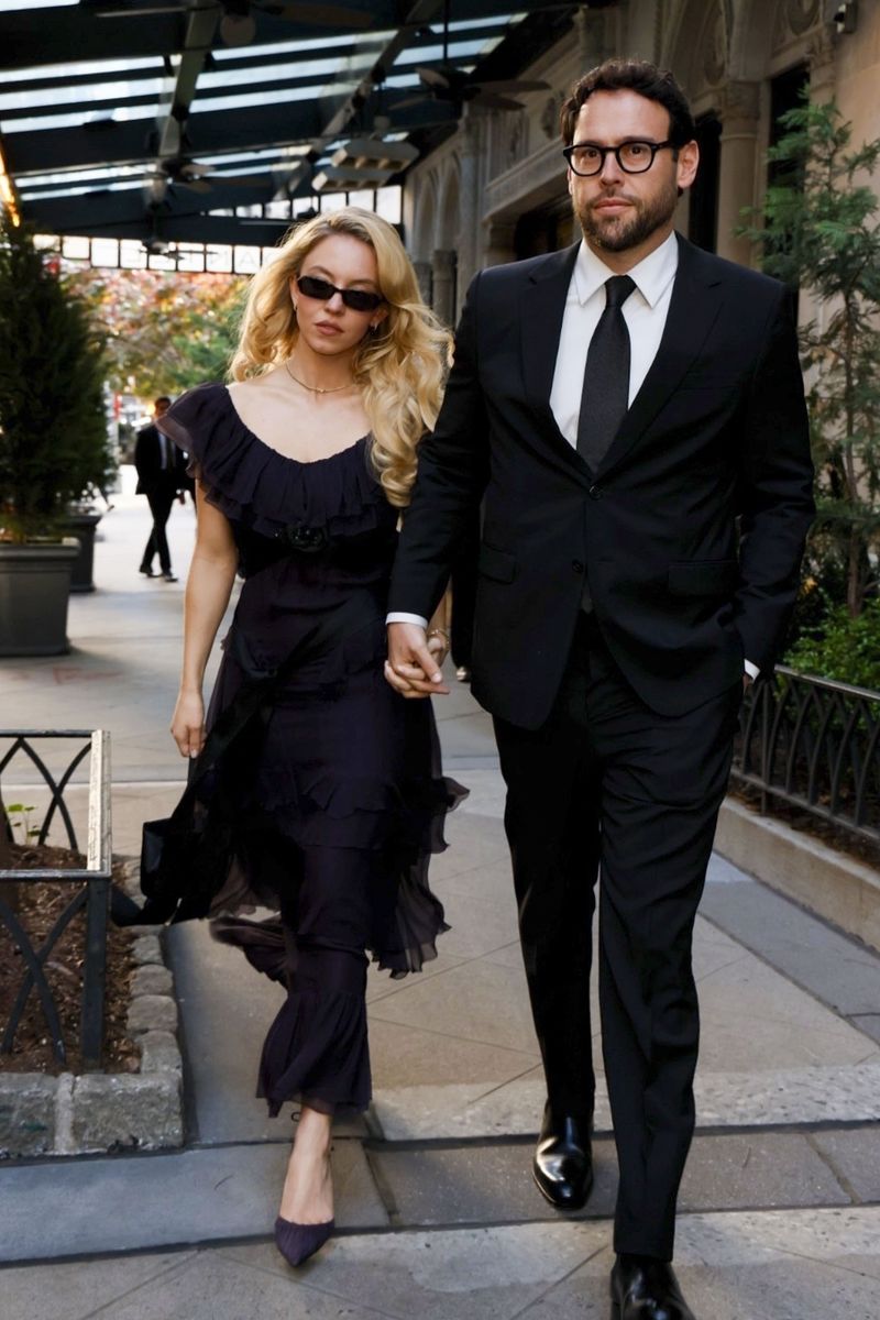 Photo © 2026 Backgrid/The Grosby Group
EXCLUSIVE
New York, NY, May 30, 2026. Sydney Sweeney and Scooter Braun were seen leaving an event at Daniel in New York City before heading to dinner together. Sweeney wore a dark navy maxi dress with layered ruffle trim along the neckline, flutter sleeves, a fitted bodice, and a flowing tiered skirt. She completed the look with pointed-toe pumps, narrow sunglasses, a delicate necklace, hoop earrings, and a structured mini handbag. Braun opted for a black suit with a black tie, square-framed glasses, and polished dress shoes.***Sydney Sweeney y Scooter Braun fueron vistos saliendo de un evento en Daniel, en la ciudad de Nueva York, antes de dirigirse juntos a cenar. Sweeney lució un vestido maxi azul marino oscuro con volantes en el escote, mangas cortas con vuelo, cuerpo ajustado y una falda escalonada de movimiento fluido. Completó el conjunto con zapatos de punta, gafas de sol estrechas, un collar delicado, aros y un mini bolso estructurado. Braun eligió un traje negro con corbata negra, gafas de montura cuadrada y zapatos de vestir pulidos.