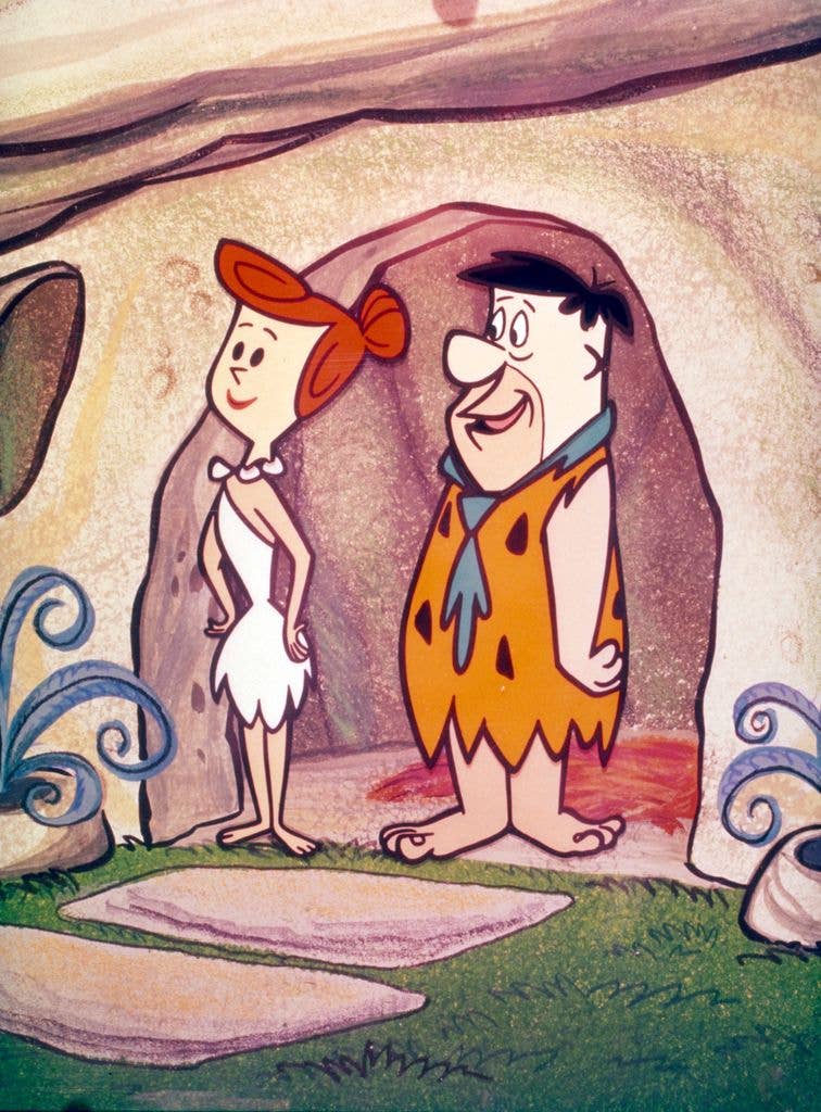 Wilma and Fred Flintstone stand in the doorway of their cave.