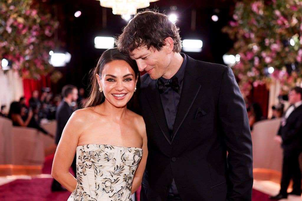 Mila Kunis and Ashton Kutcher standing together, smiling, at a formal event.
