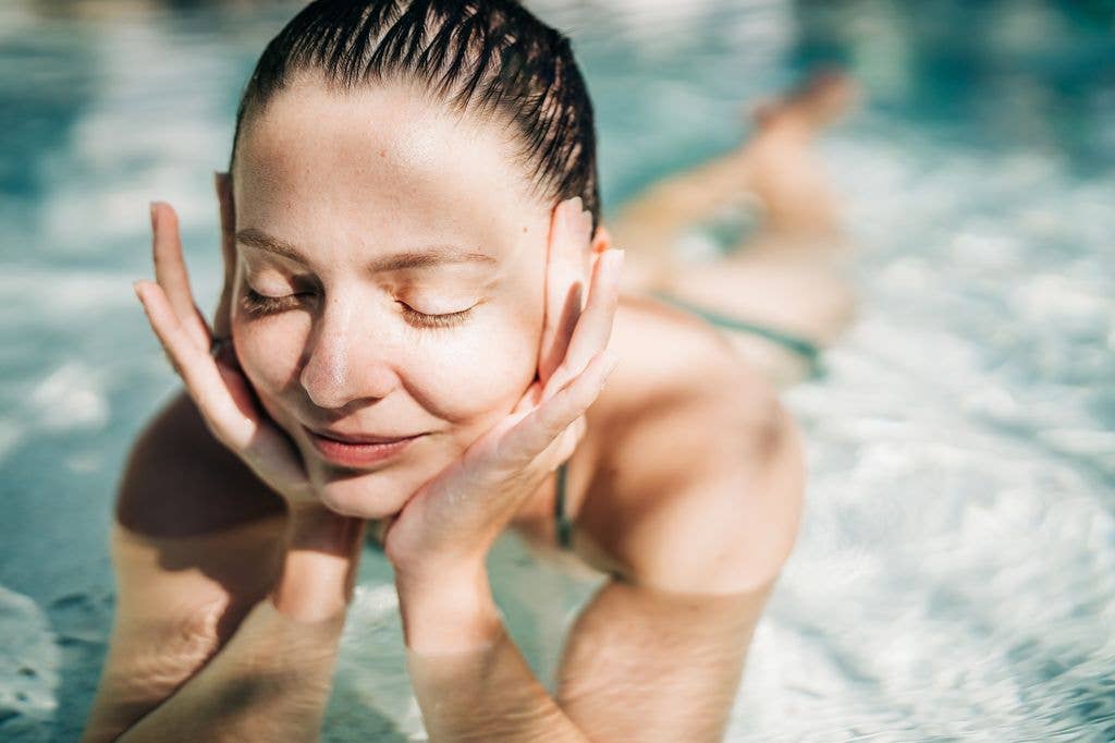 A young woman lies in a swimming pool, leaning on her hand with soft sunlight on her face. Her tranquil expression and the serene water create a peaceful and relaxed atmosphere, perfect for representing leisure and vacation.