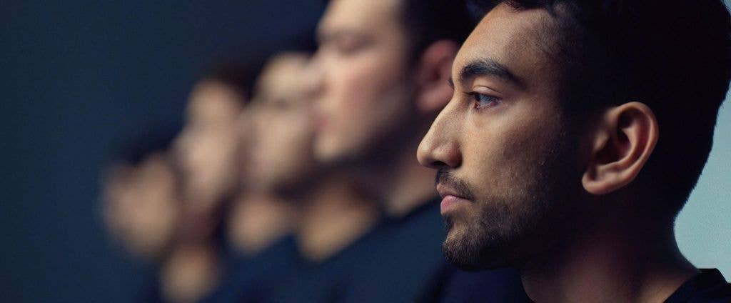 A man with a beard and short hair stands in front of a blurred line of people.