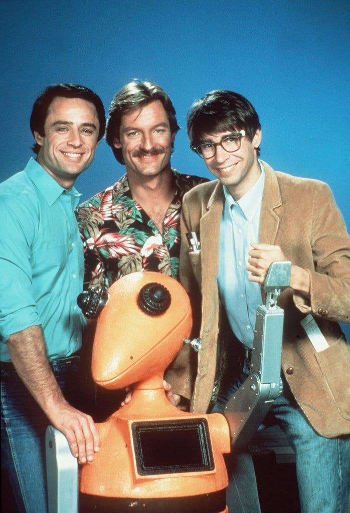 Perry King, Joe Penny, and Thom Bray stand with a robot, smiling.
