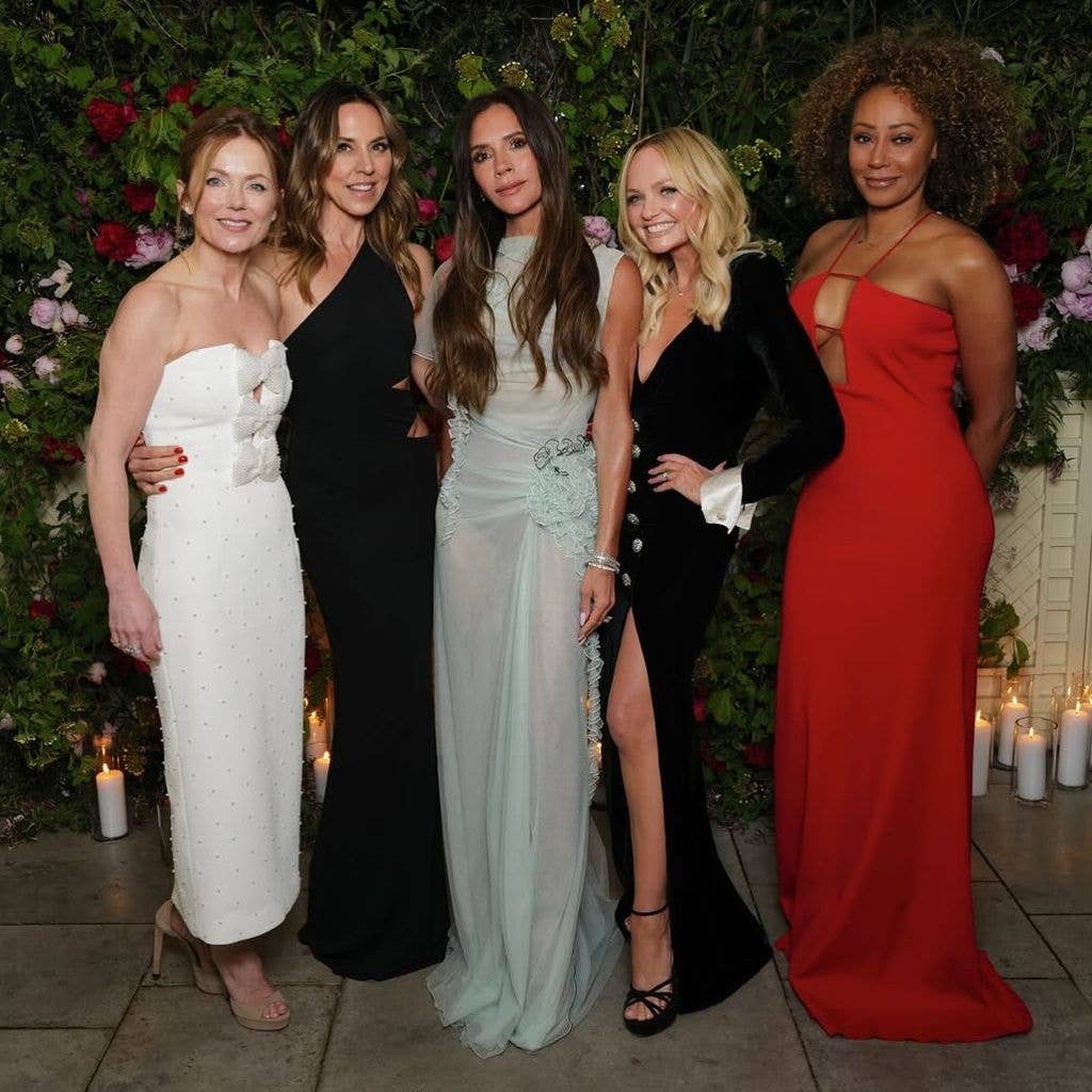 Five women, including Melanie C, Victoria Beckham, and Geri Halliwell, pose together in elegant dresses in front of a floral backdrop.