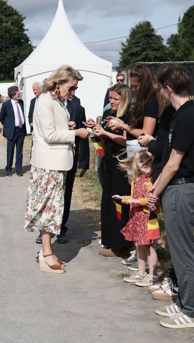 The Belgian queen completed her countryside chic ensemble with a raffia handbag, statement earrings and oversized sunglasses.