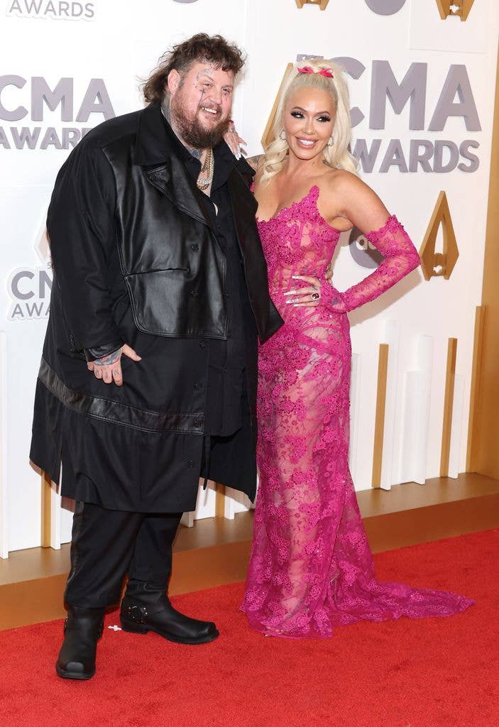 Jelly Roll and Bunnie Xo in pink gown smiling on red carpet at CMA Awards.