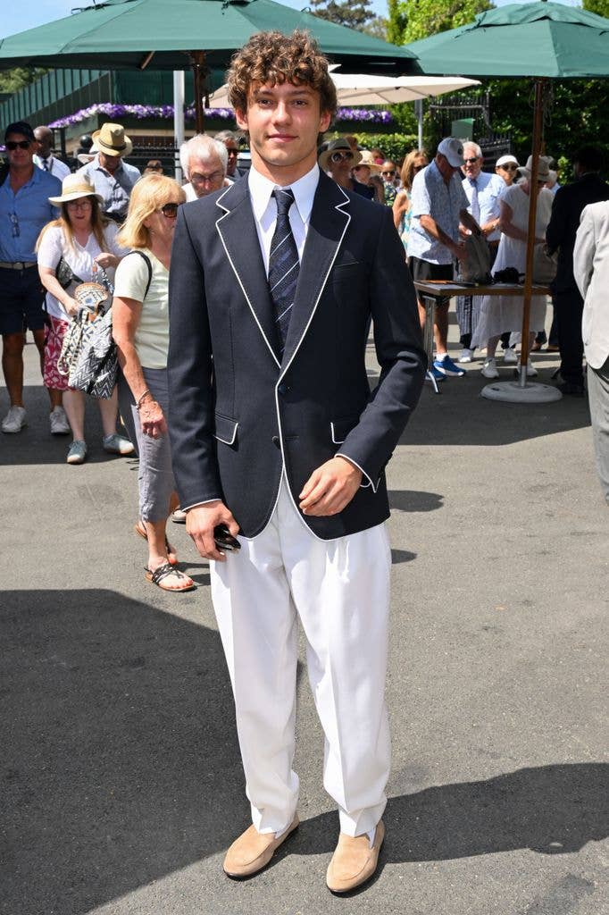 Andrea Kimi Antonelli in black blazer and white pants stands in crowd, no visible celebrities.