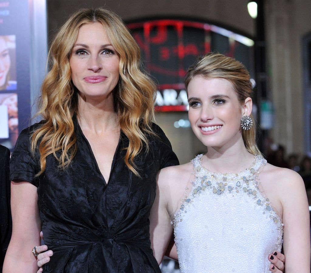 Julia Roberts wears a black dress with her arms around Emma Roberts, who is wearing a white sparkly dress.