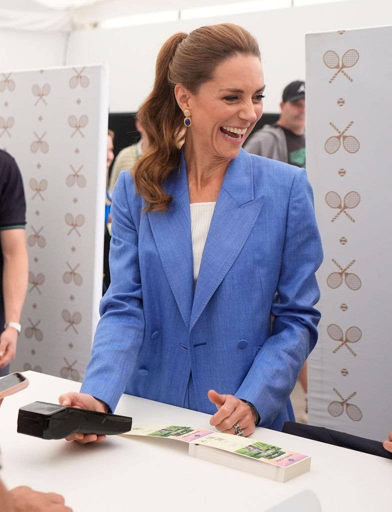 Kate Middleton in a blue blazer, smiling and holding a scanner at a table.