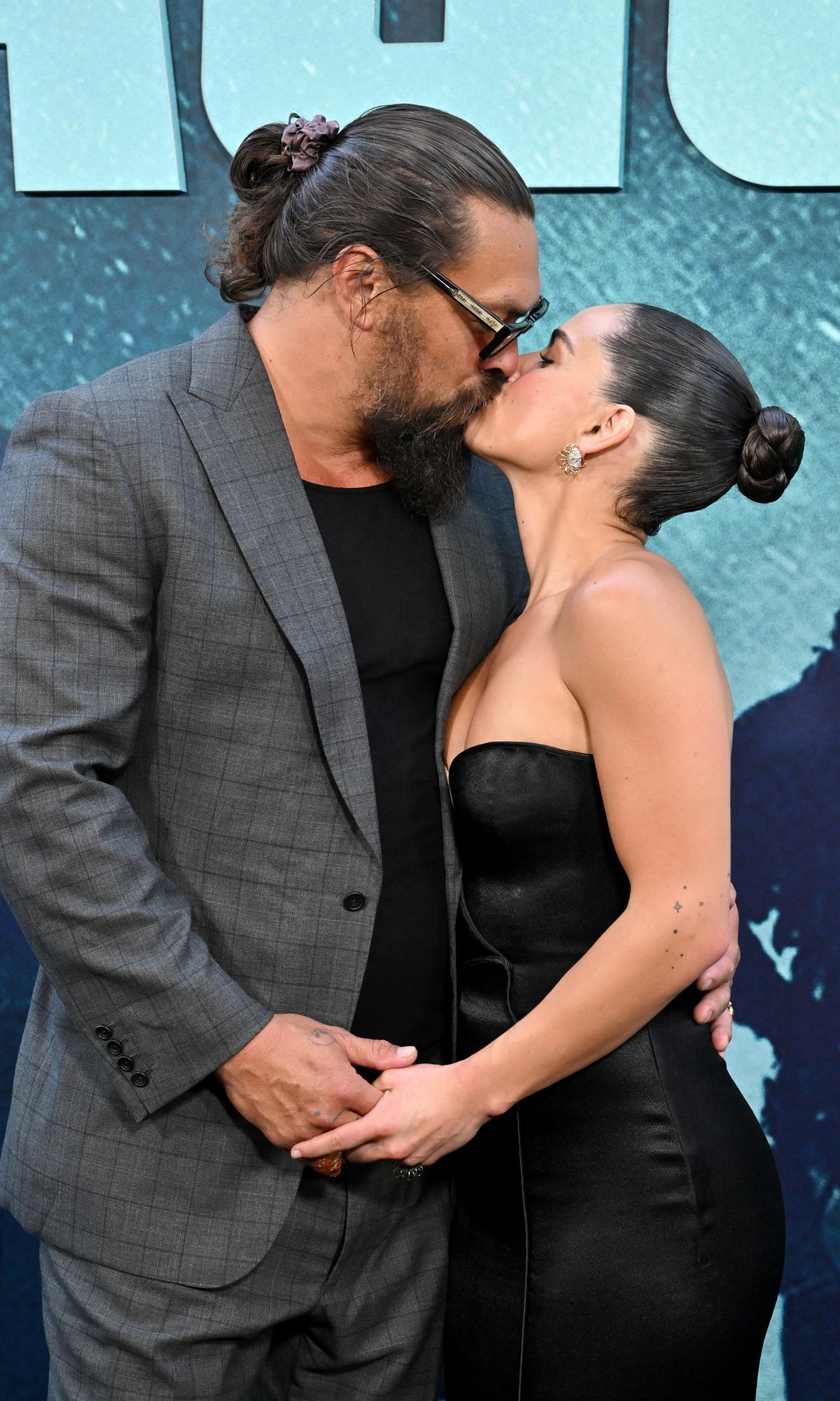 Jason Momoa and Adria Arjona sharing a kiss on the red carpet