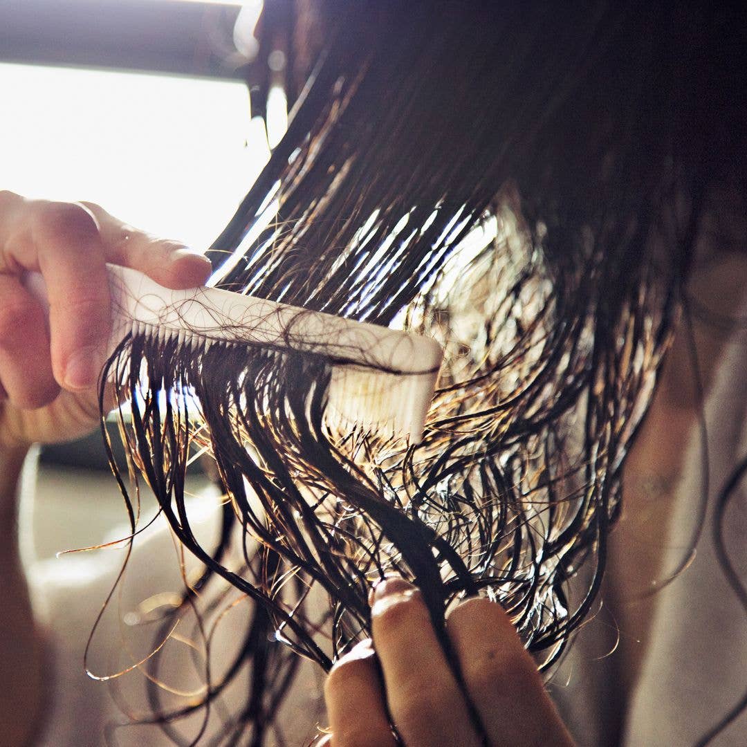 Closeup of the hands of a woman who has taken a shower and is combing her wet hair. Image located in the bathroom of a home with sunlight coming through the window.The comb is full of tangled hair.