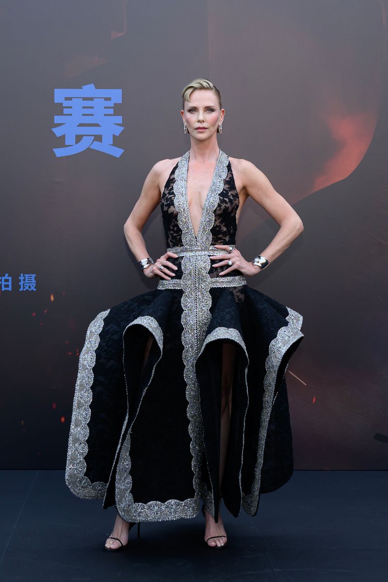 Charlize Theron pairs her bold new haircut with a striking black sheer lace gown featuring a plunging neckline, sculptural skirt and elegant silver embellishments during The Odyssey press tour in Beijing.