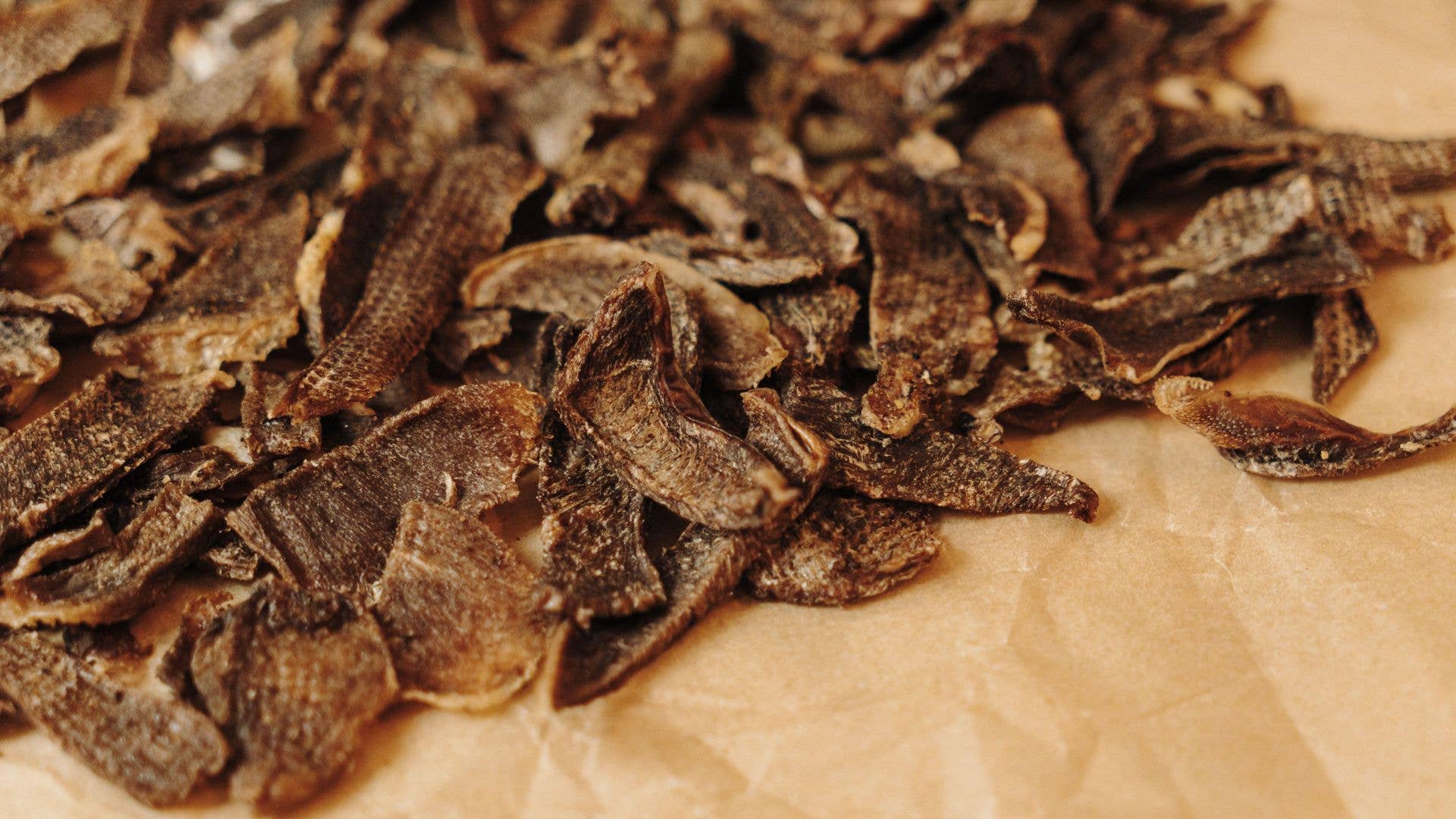 Pile of dried, brown, crispy food pieces on a beige paper surface.