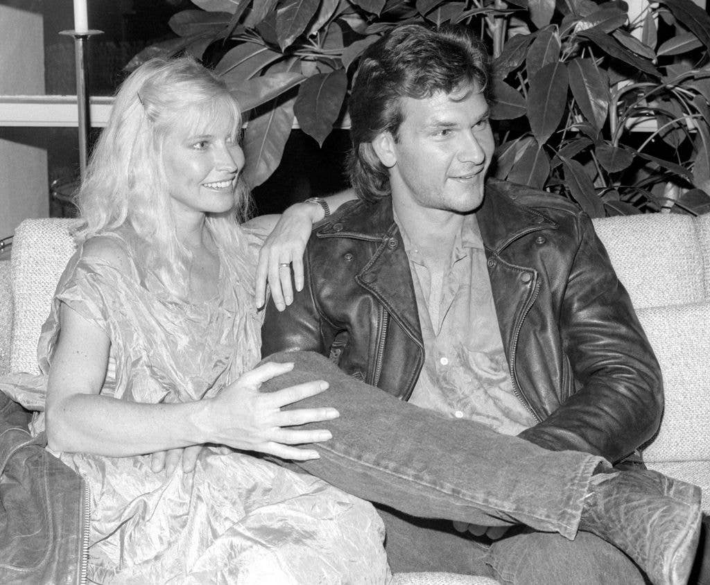 Lisa Niemi rests her arm on Patrick Swayze's shoulder and holds the knee of the leg he has propped up. They both smile and look to the right of the image.