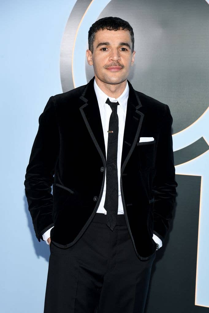 Christopher Abbott stands in a black velvet suit and tie, hands in pockets.