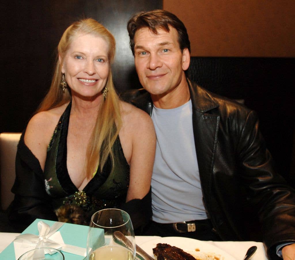 Lisa Niemi and Patrick Swayze sit close together, Patrick holding an arm around Lisa's back while sat at a table.