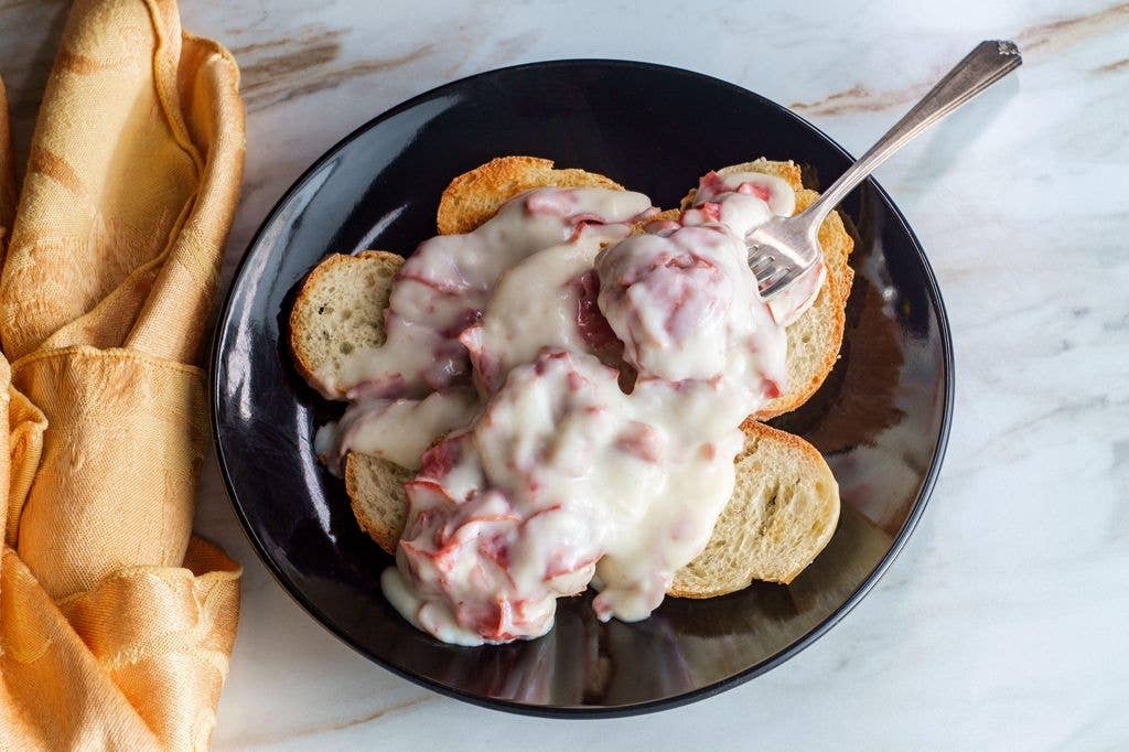 A plate of open-faced sandwiches with white sauce and meat, served with a fork