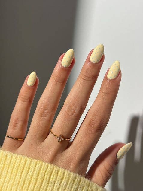 Minimalist polka dot nail design using butter yellow base with tiny baby blue dots on oval shaped nails