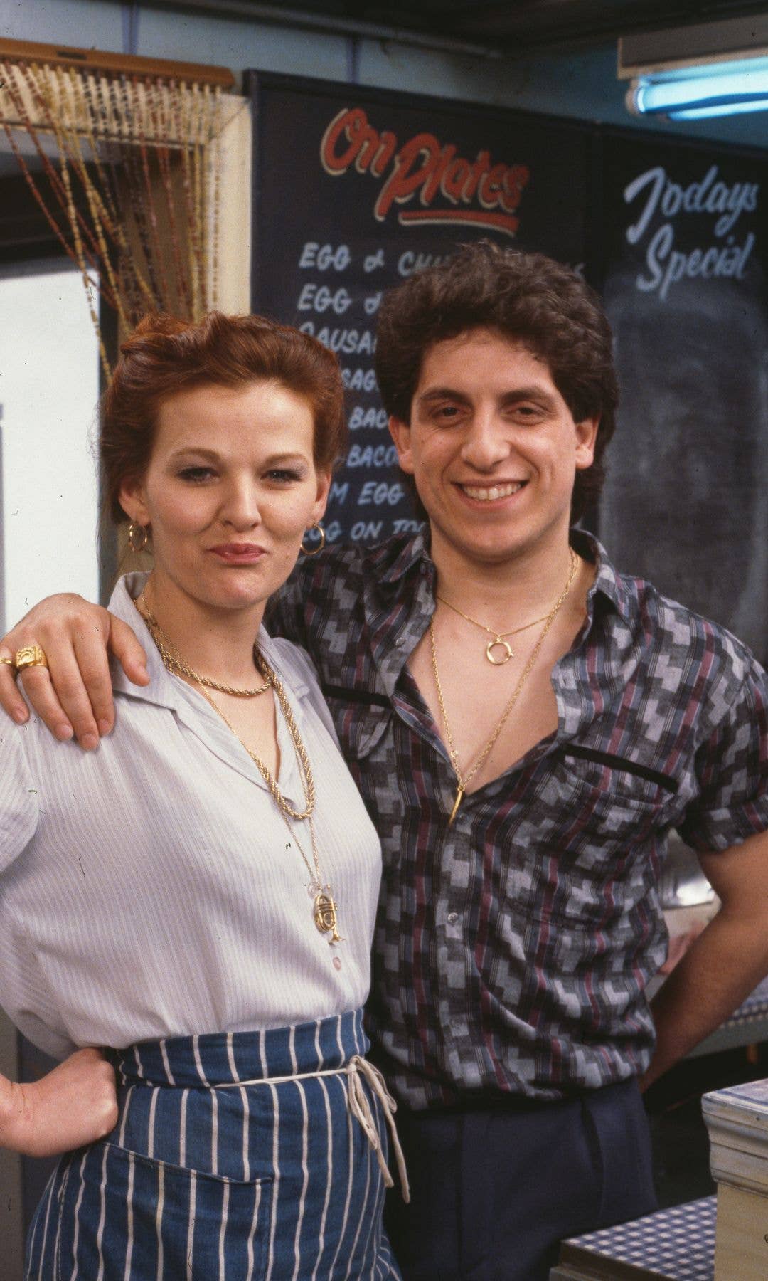 A man and a woman stand together, smiling, in a restaurant setting.