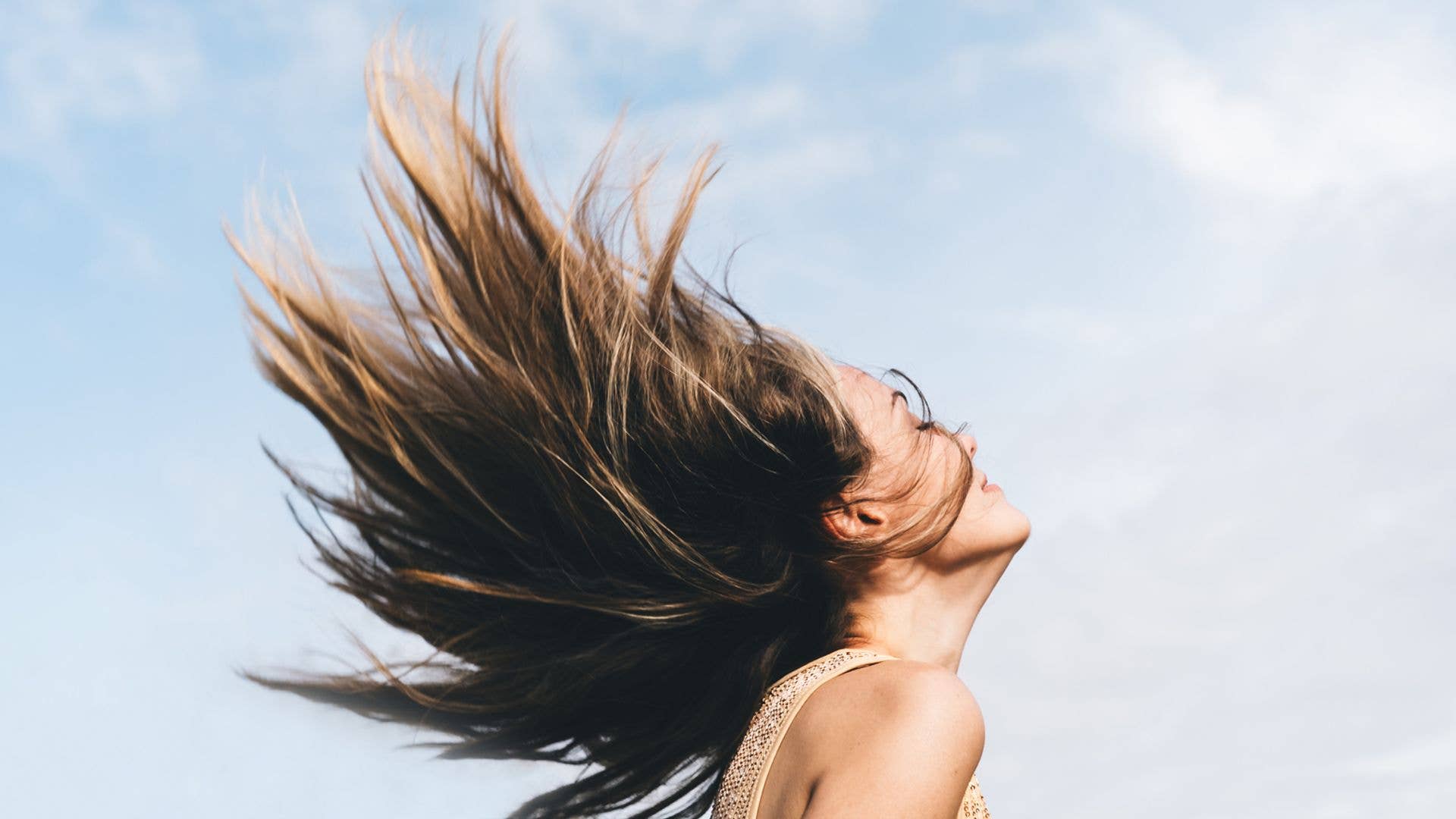 Dynamic portrait of a woman flipping her hair against a bright sky. The motion captures freedom, vitality, and lightness, with natural light emphasizing movement and self-expression.