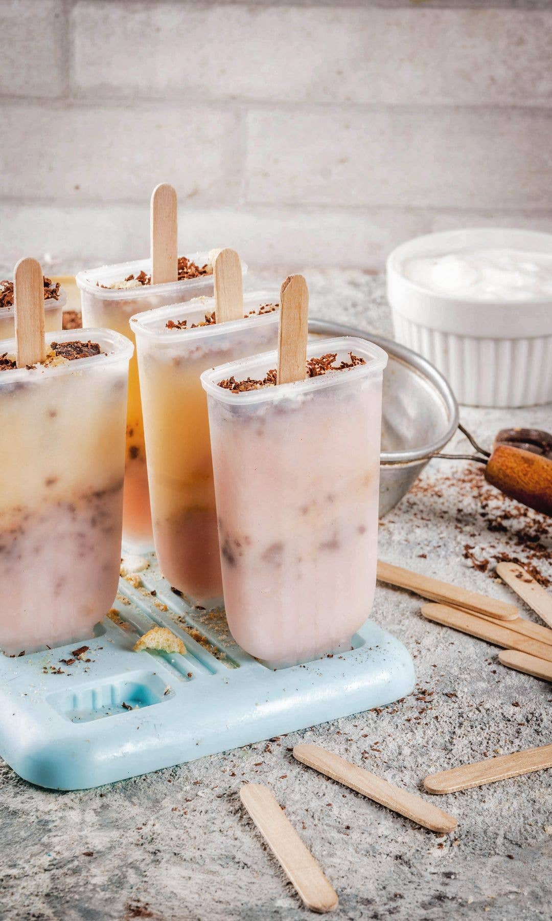 Four popsicles with wooden sticks on a blue tray, surrounded by extra sticks and ingredients.