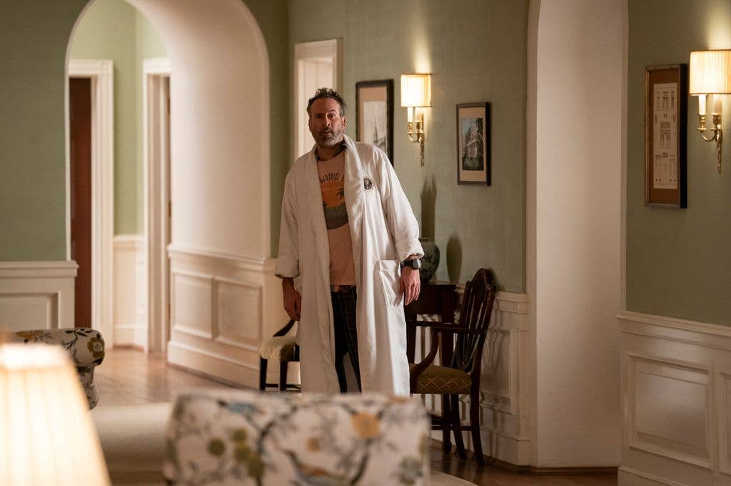 Jason Lee stands in a hallway wearing a white robe over a patterned shirt.