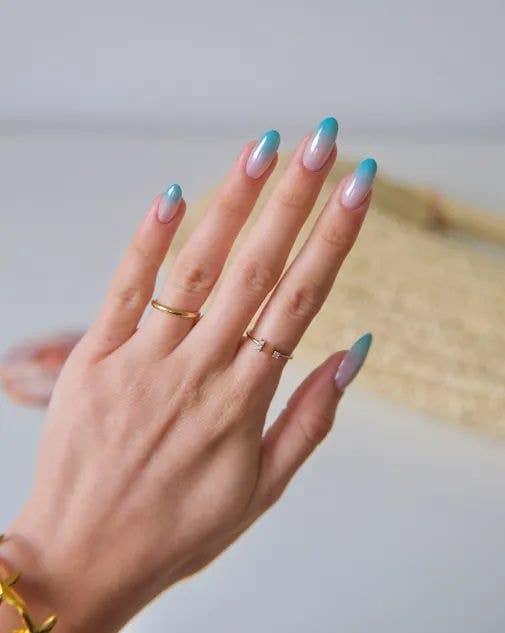 A person's hand with blue and white nail polish, gold rings, and bracelets.