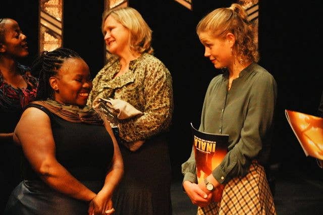 Four women on stage, two holding books, smiling and conversing.