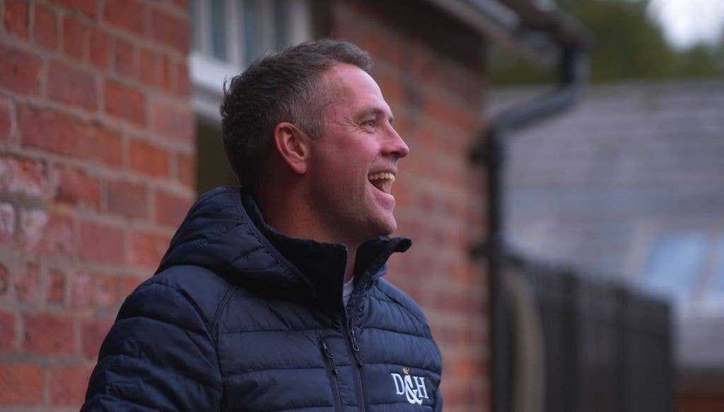 Michael Owen, wearing a navy blue D&H jacket, smiles broadly outside a brick building.