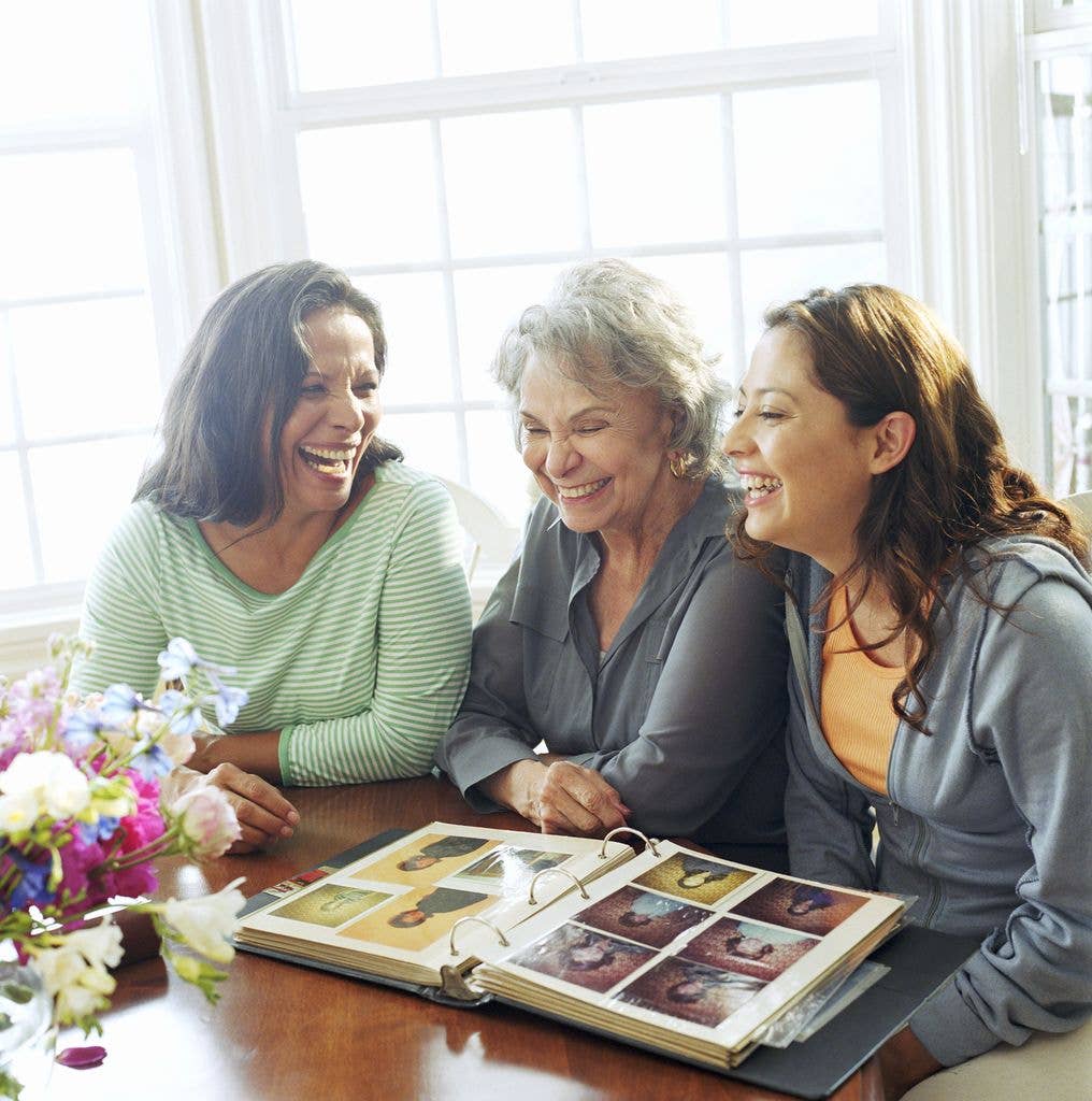 Three women sitting at a table, smiling and looking at a photo album.