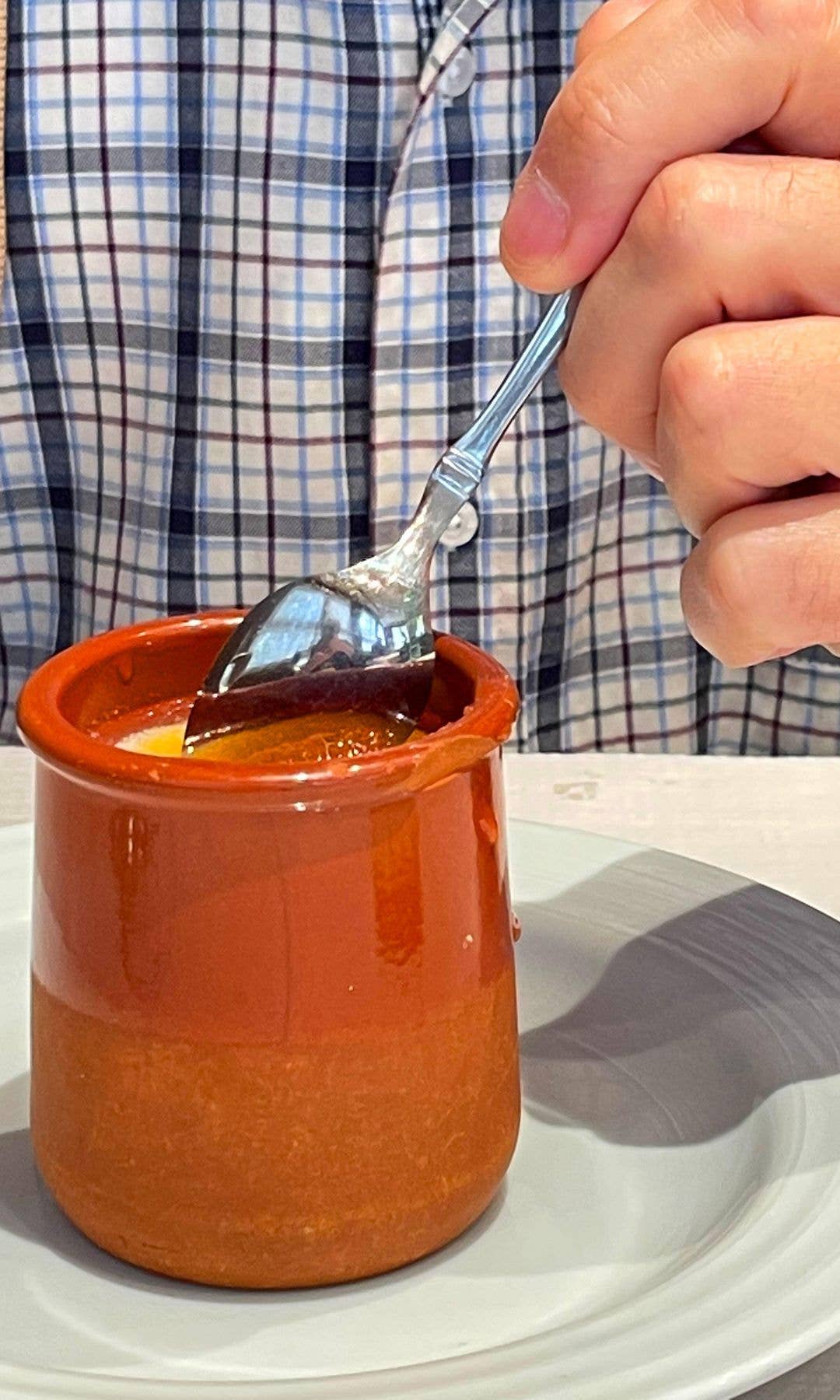Person in plaid shirt holding a spoon over a small orange bowl of food.