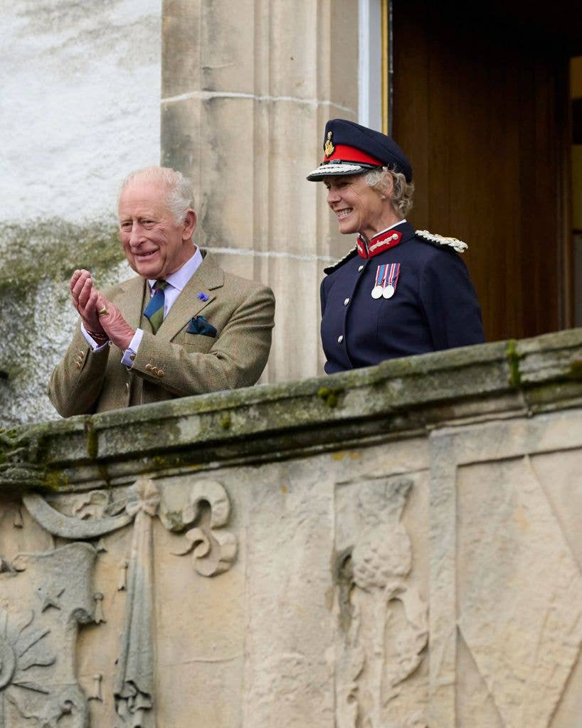 King Charles clapping beside a woman in military uniform on a balcony.