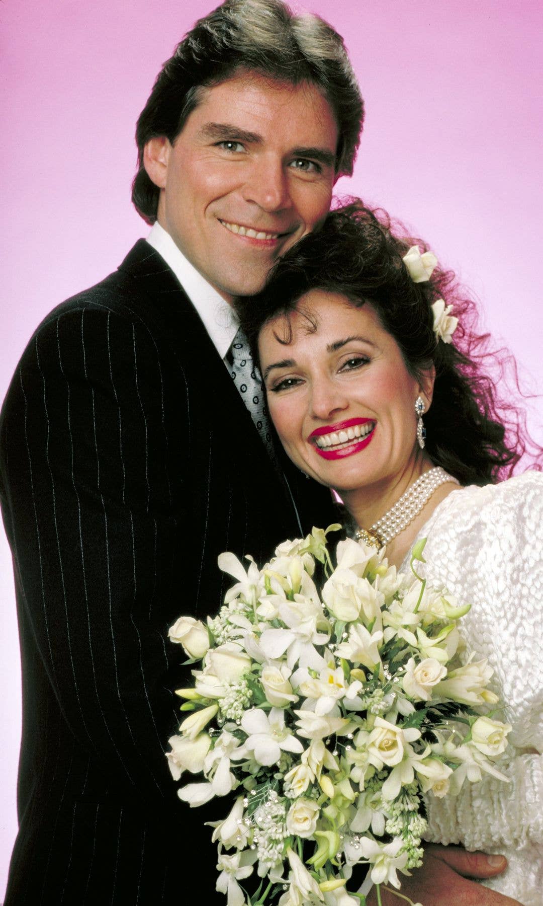 Susan Lucci in a white gown holding a bouquet, posing with a man in a black suit.