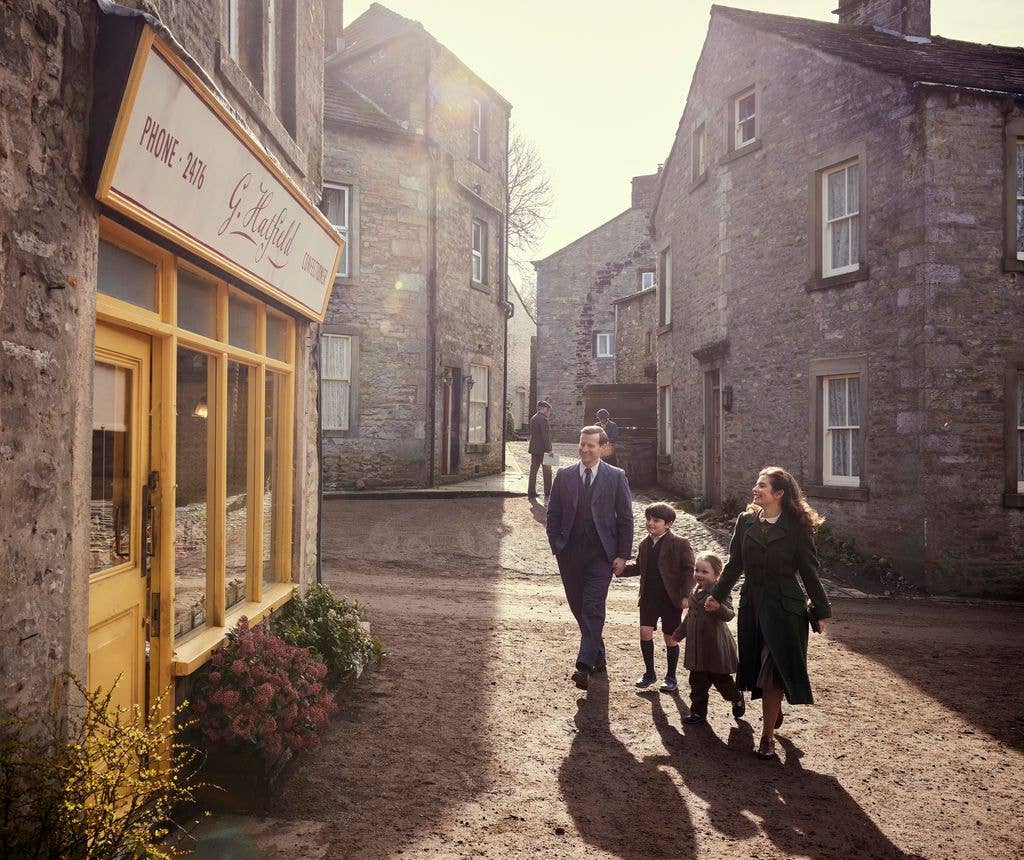 Family of four, including two children, walks down a cobblestone street in a quaint village setting.