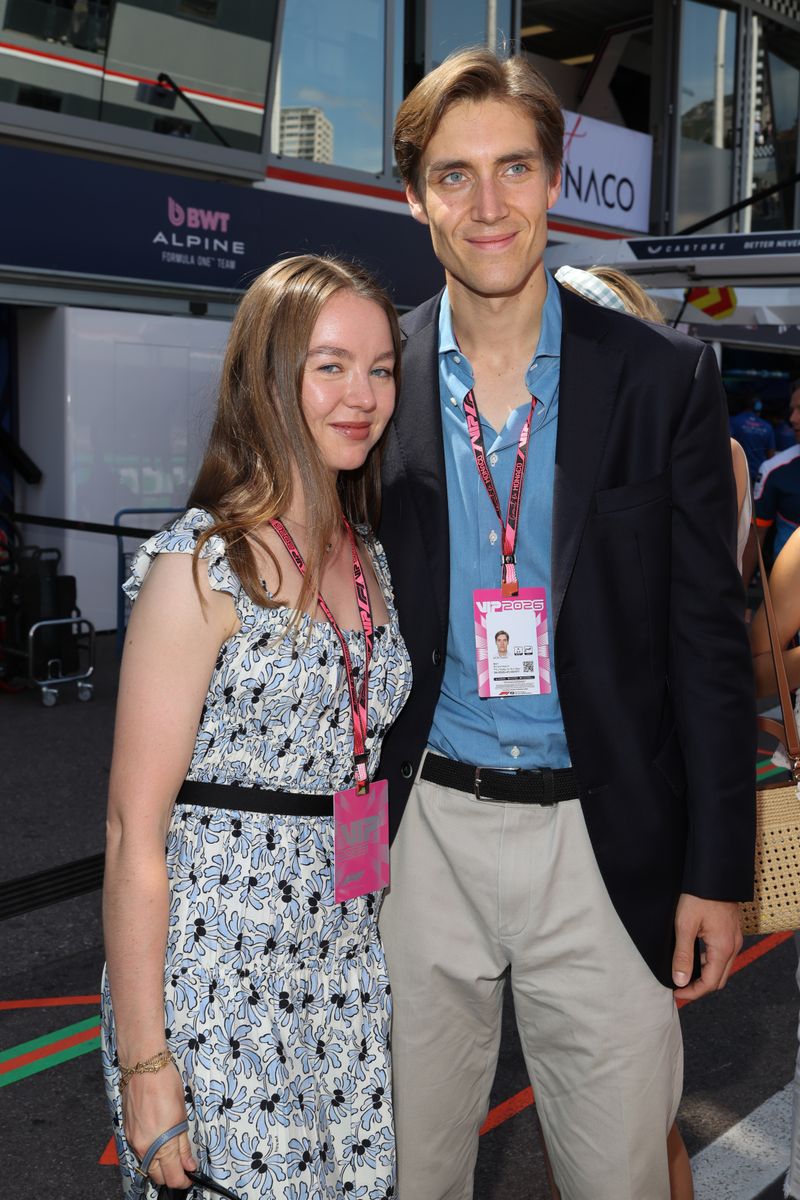 Alexandra de Hannover in a blue-and-white floral dress and Ben-Sylvester Strautmann in a navy blazer and blue shirt stand close together in the Formula 1 paddock, both wearing pink VIP 2026 lanyards, with BWT Alpine and Monaco signage visible behind them.