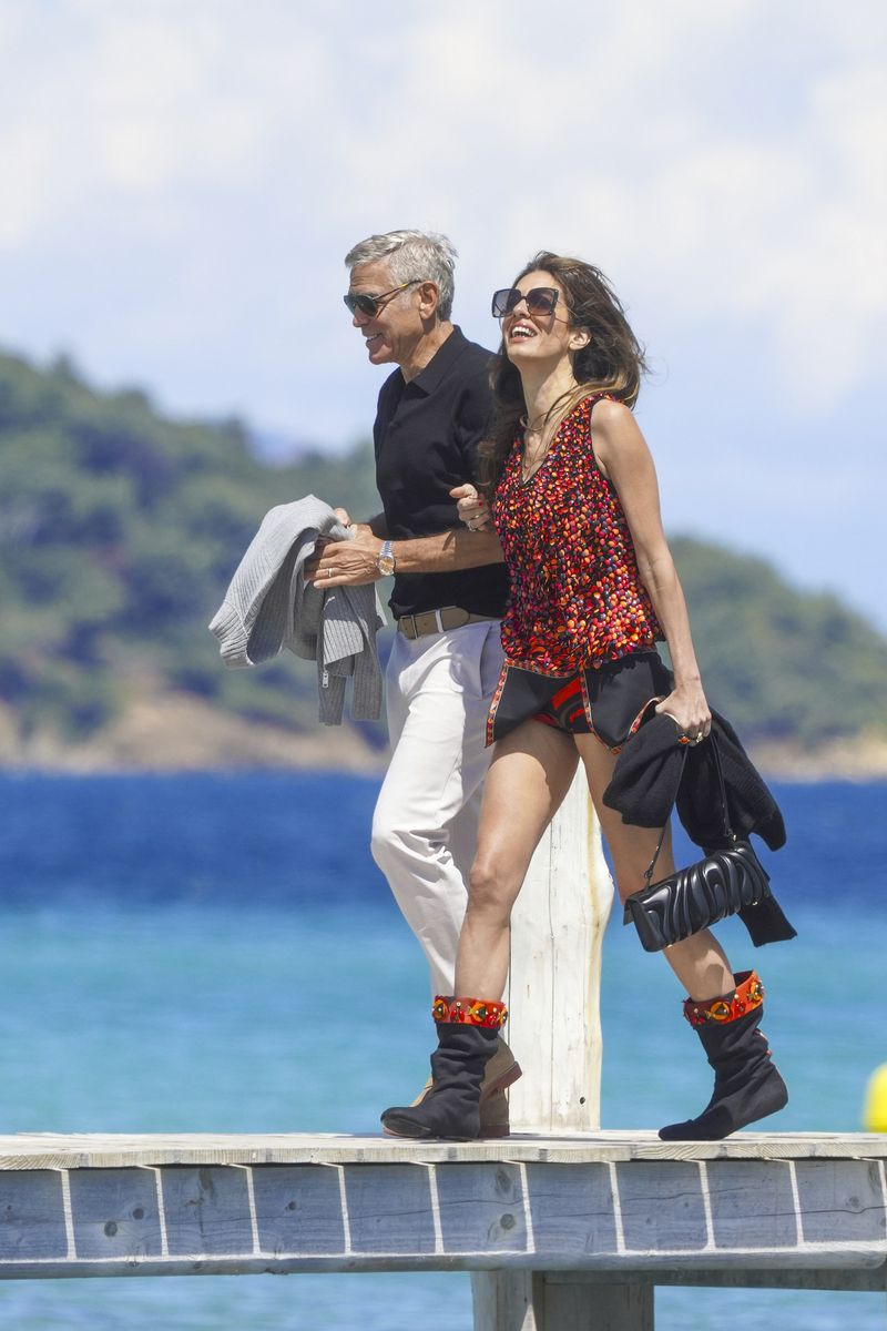Amal completed the look with statement black boots adorned with colorful accents, oversized sunglasses, and a quilted black handbag that elevated the outfit with a touch of modern glamour.