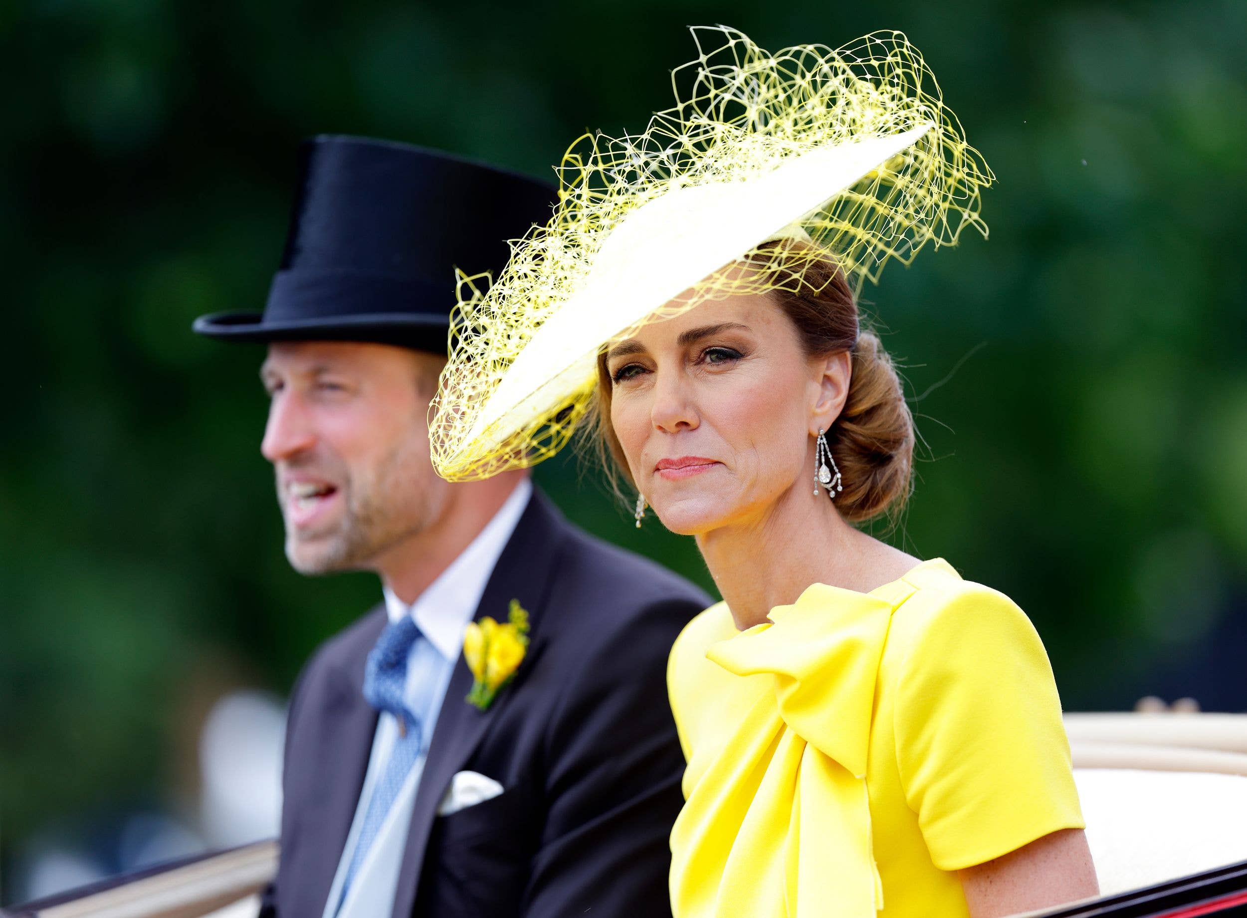 Prince William in a black suit and top hat, sits beside Kate Middleton in a yellow dress and hat