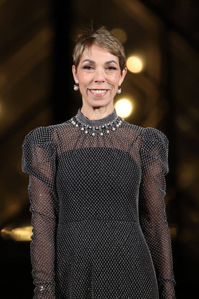A smiling woman with short hair wearing a black, sparkling dress and pearl necklace.
