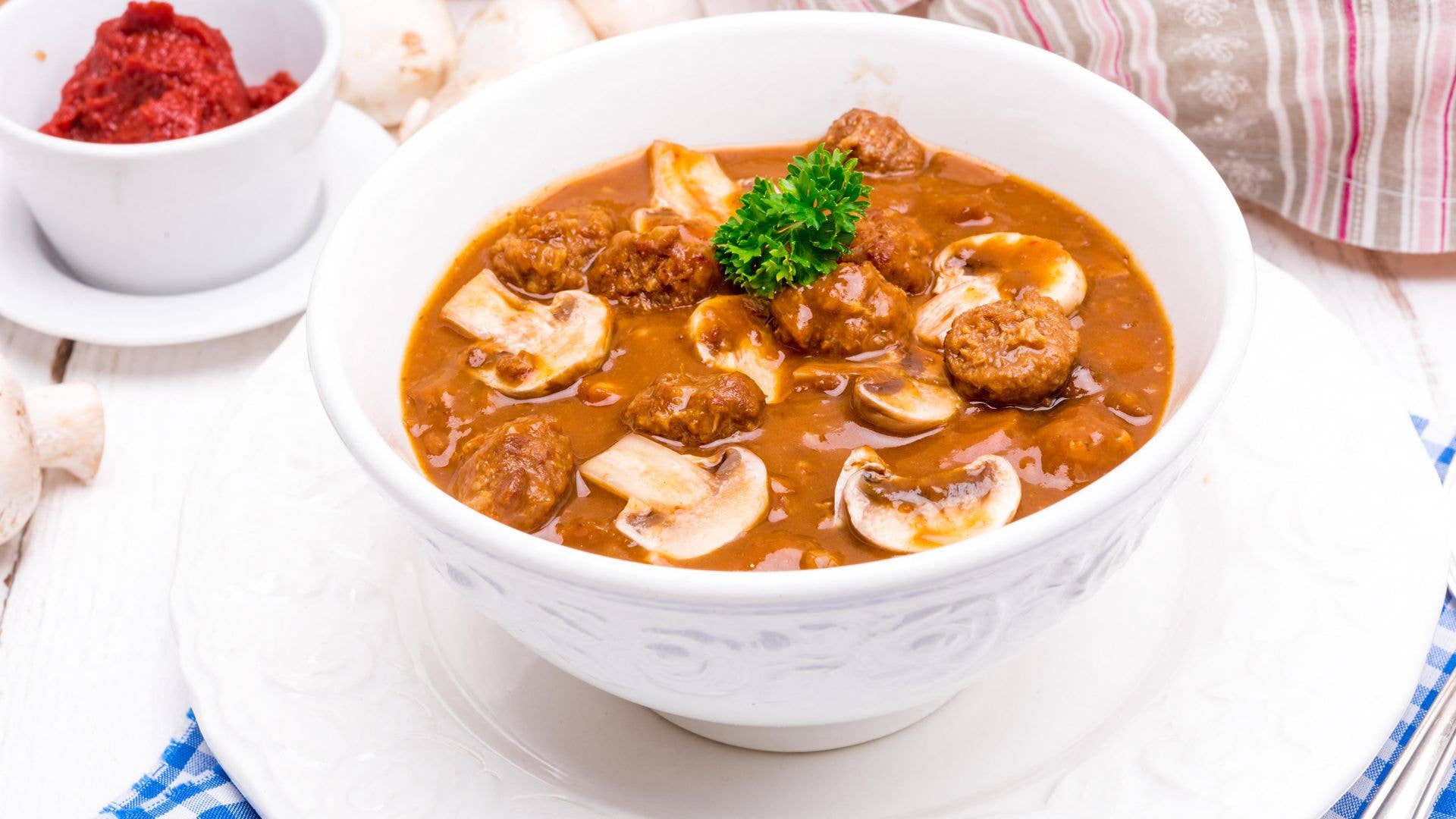 White bowl of mock turtle soup with parsley on a white plate.