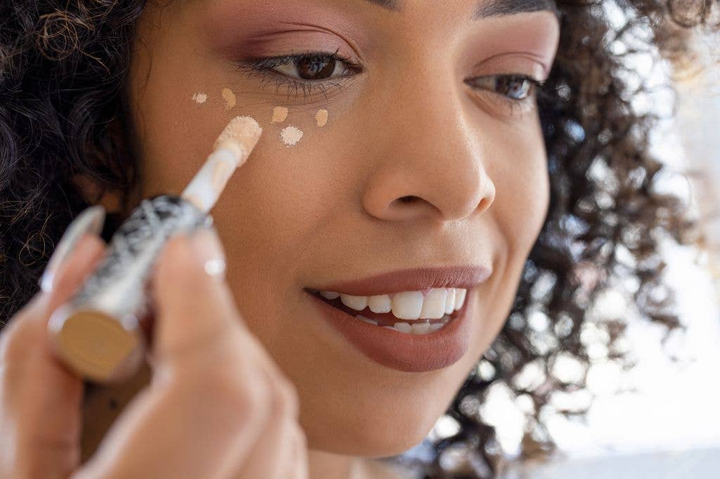 woman applying peach color correcting concealer.