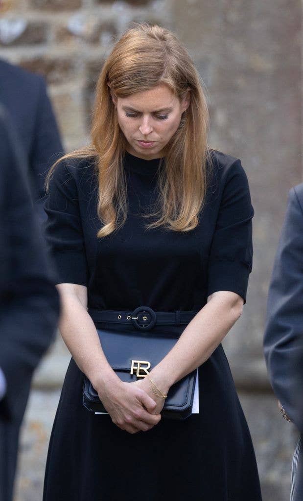Princess Beatrice looking down, wearing a black dress and holding a black clutch.