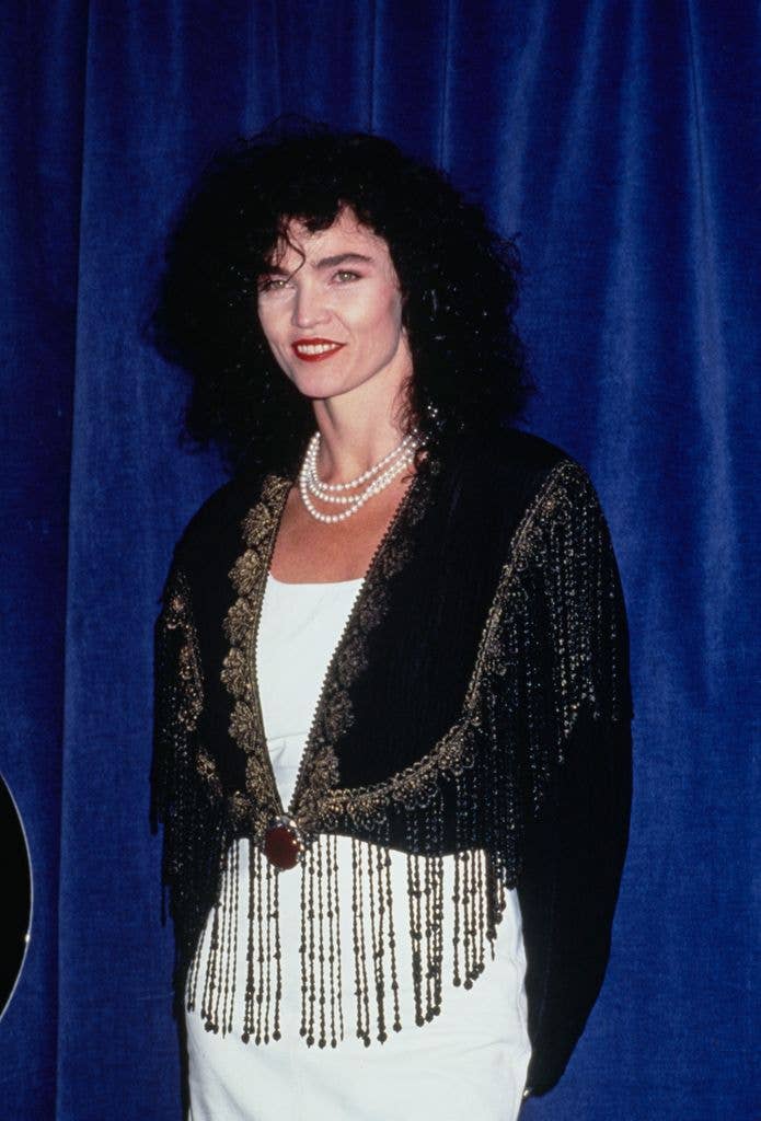 Alannah Myles smiling, wearing a white dress and black fringed jacket.