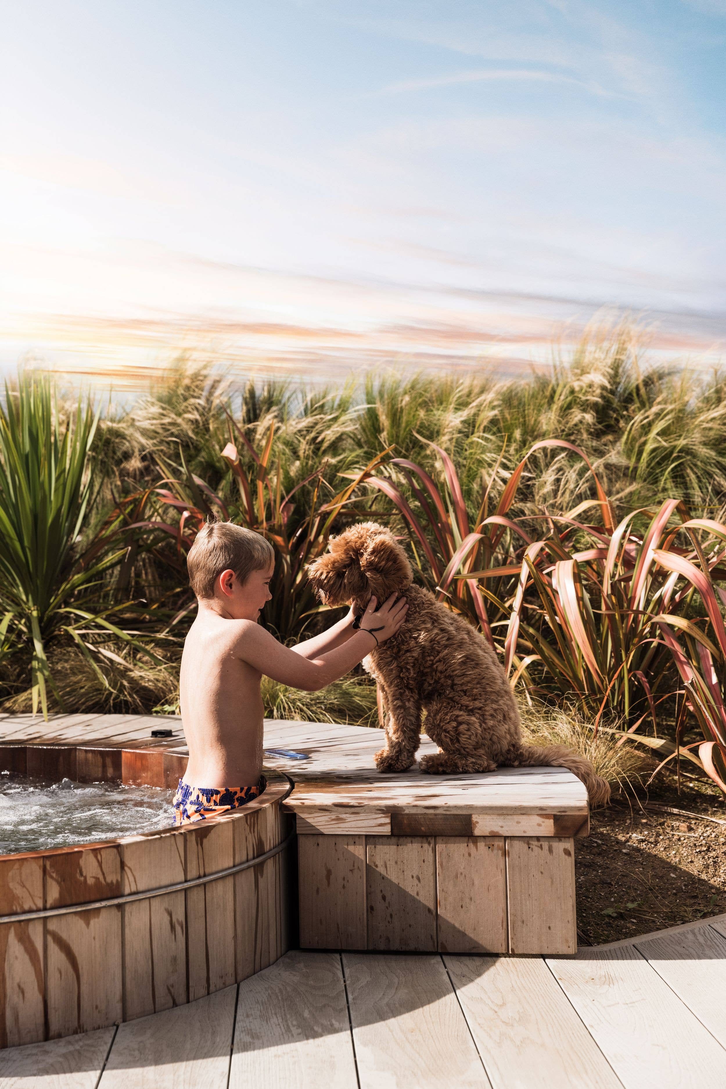 Three Mile Beach: a child is in the hot tub, stroking his dog that sits on the edge